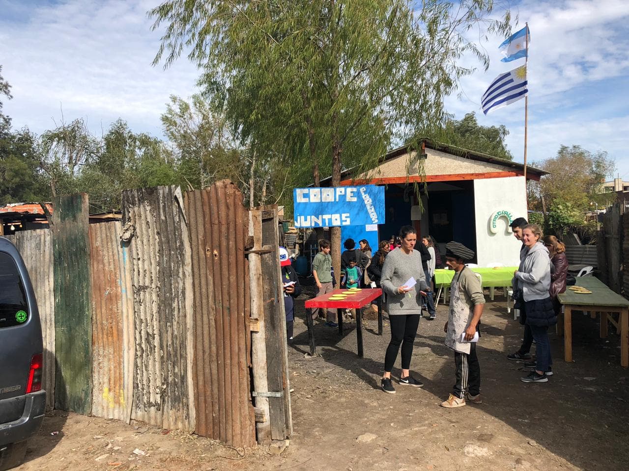Grupo de personas de pie alrededor de una mesa al aire libre, disfrutando de un momento juntos.