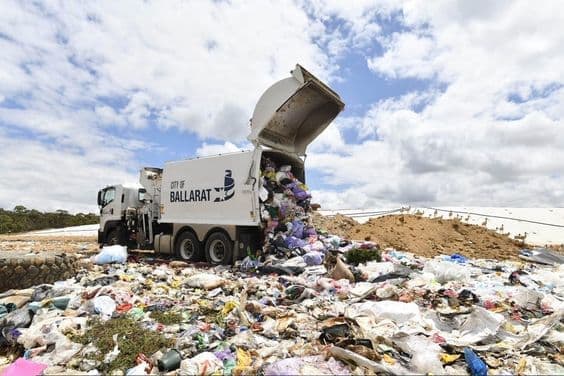 Un camión de basura está vertiendo desechos en el suelo, formando un gran montón de basura.